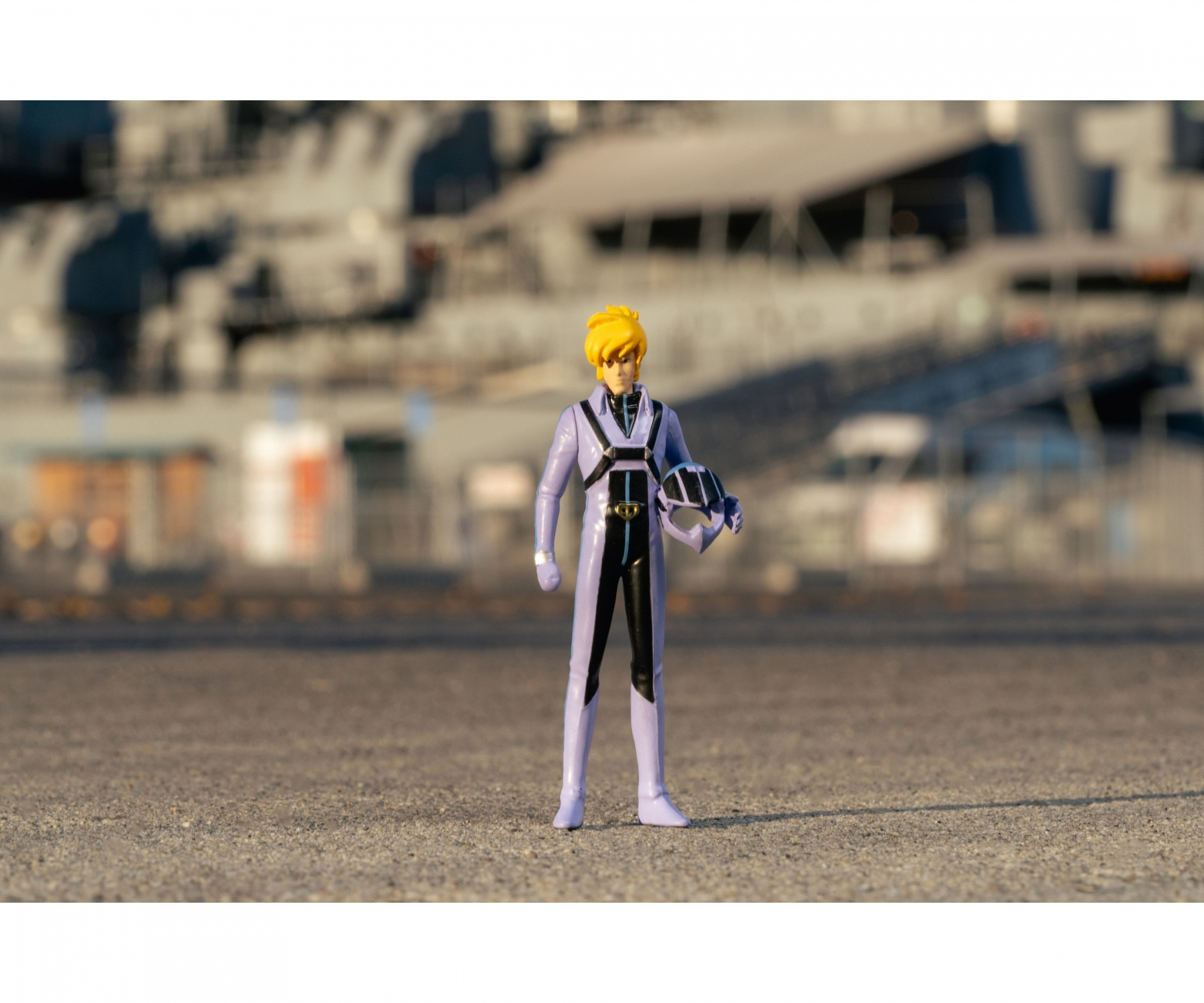 Figurka w fioletowym kombinezonie trzymająca hełm, stoi na asfalcie.