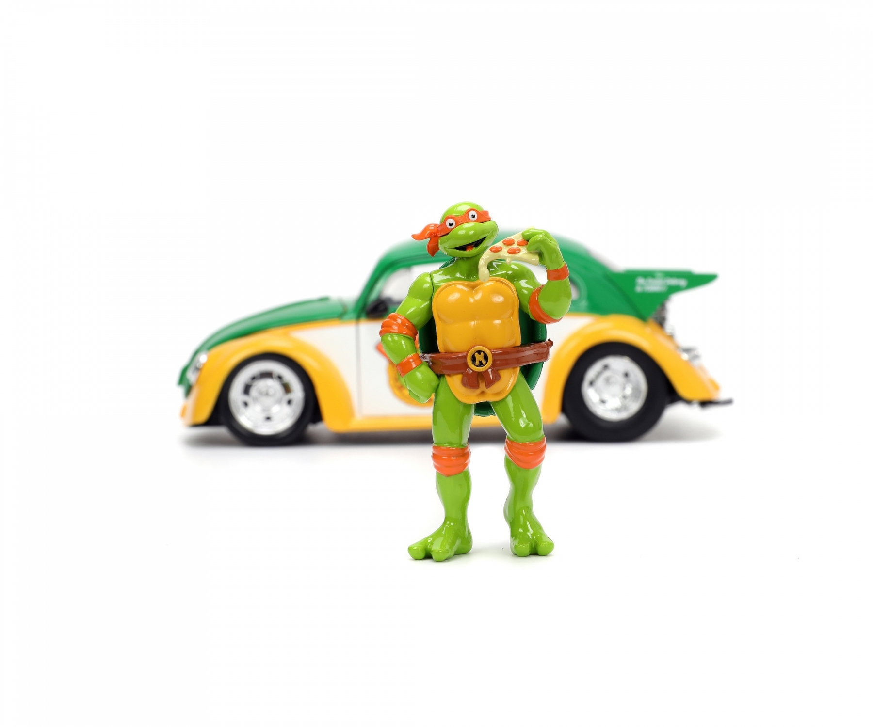 Teenage Mutant Ninja Turtle Spielzeug hält Pizza, mit einem Käfer-Auto im Hintergrund.