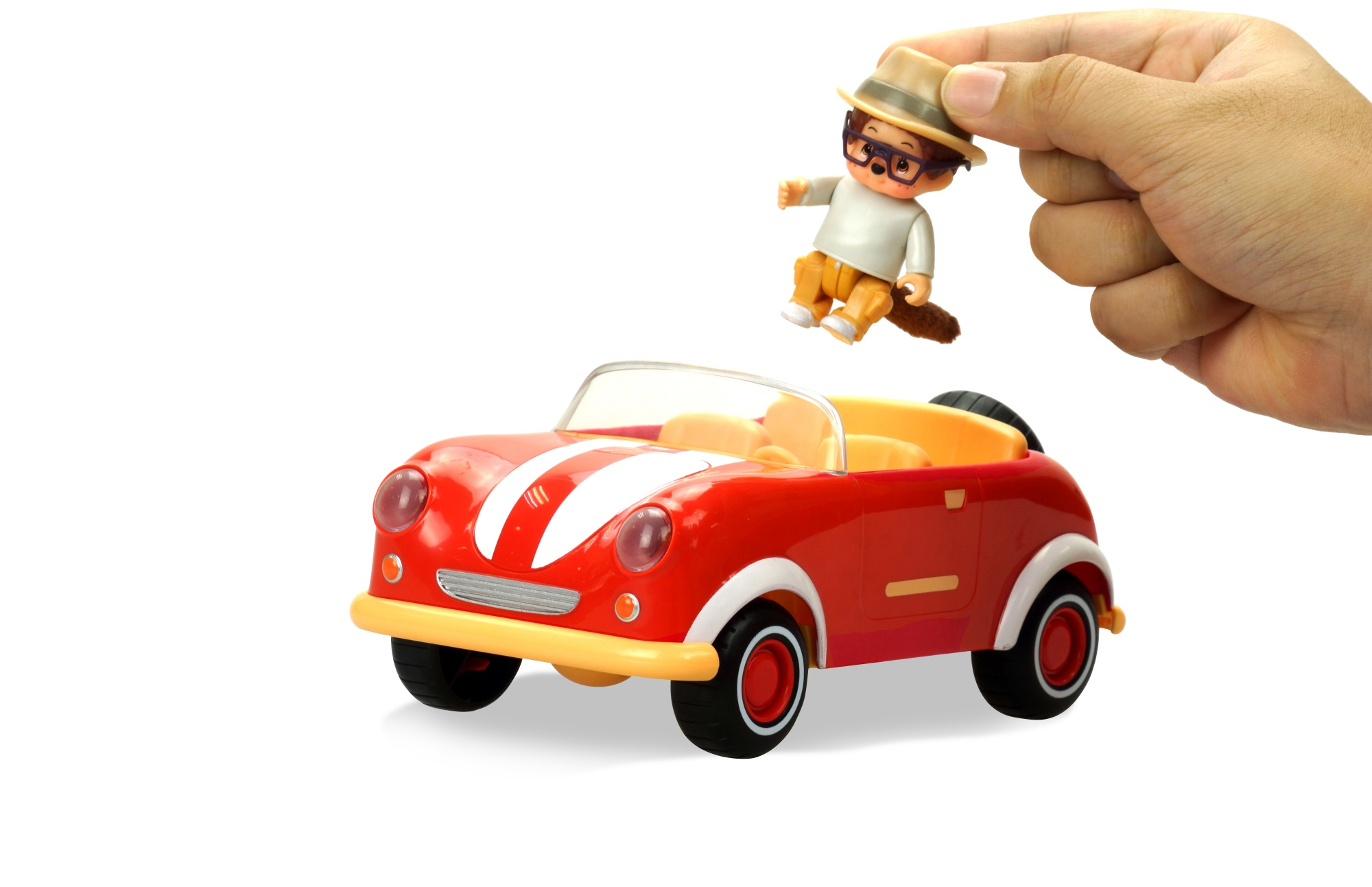 Una mano sostiene una figura de juguete sobre un coche de juguete rojo con rayas blancas. El coche está sobre un fondo blanco.