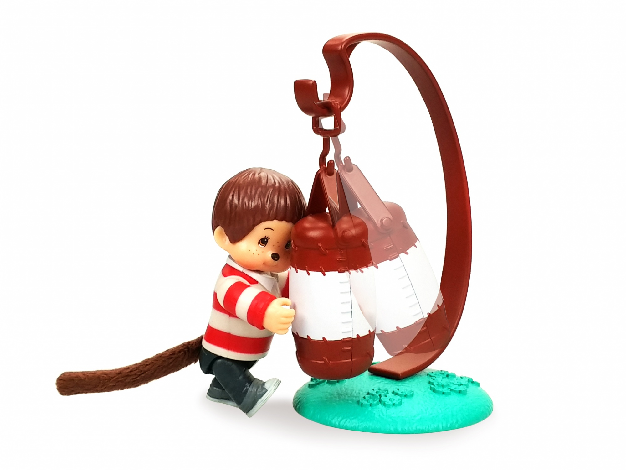 Figurka zabawki małpy z koszulą w czerwone paski, stojąca obok worka treningowego na stojaku. Białe tło.