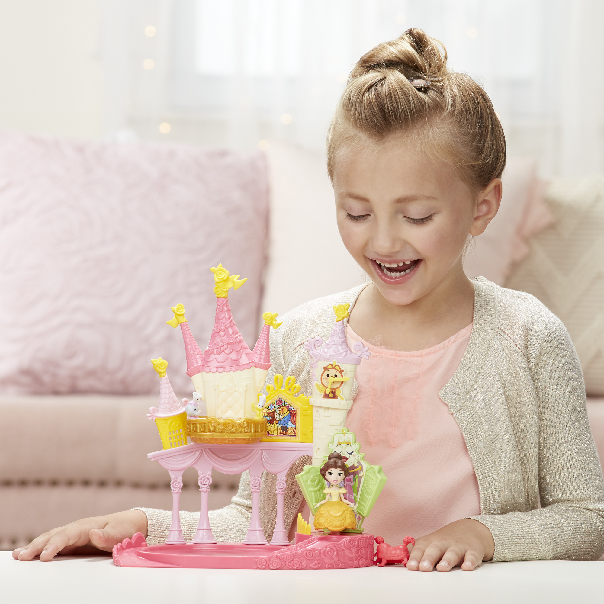 Una bambina sorride a un castello giocattolo. Il castello è rosa e giallo con personaggi Disney.
