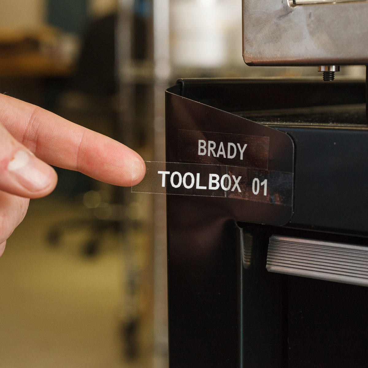Palec wskazuje na etykietę na czarnej szafce. Etykieta głosi 'BRADY TOOLBOX 01'.