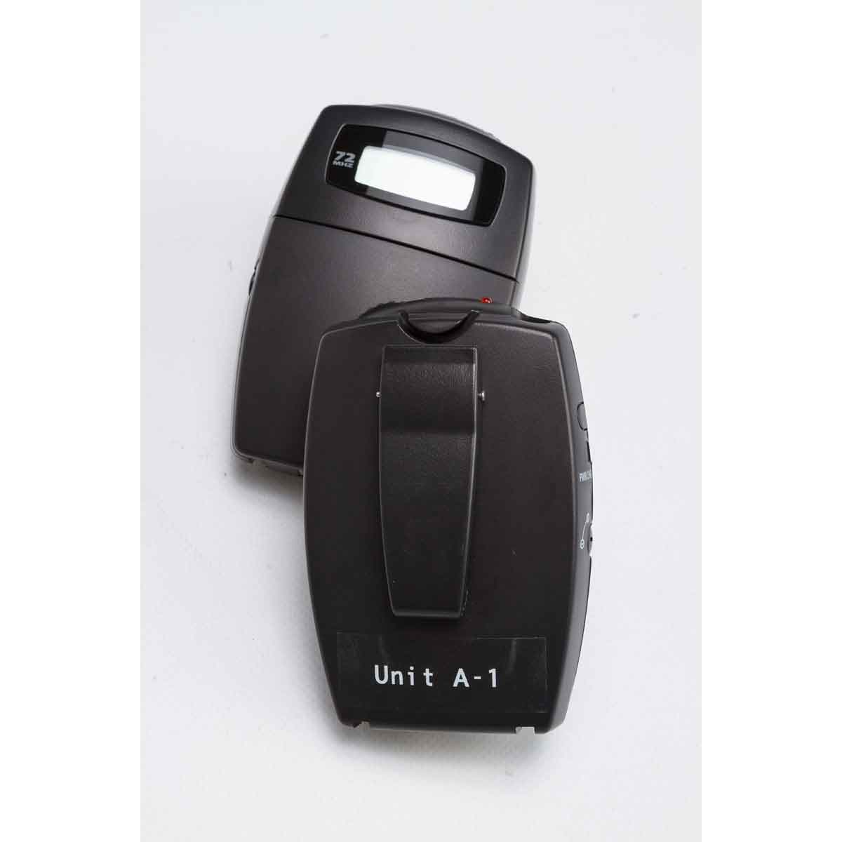 Dwa czarne, prostokątne urządzenia komunikacyjne, prawdopodobnie krótkofalówki, ułożone jeden na drugim. Białe tło.