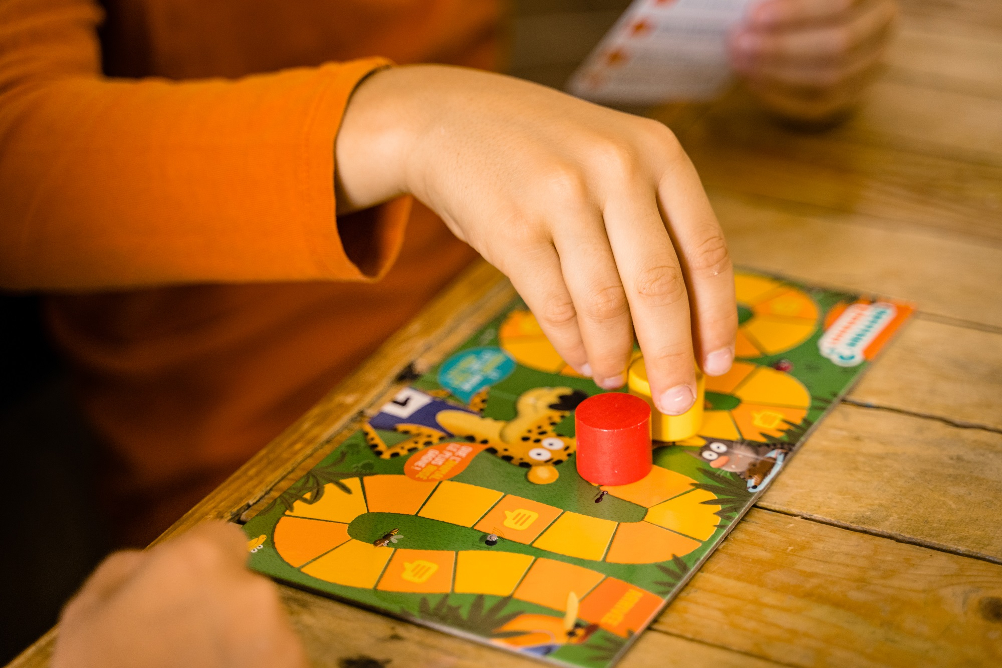 Ręce grające w grę planszową z kolorowymi drewnianymi pionkami na drewnianym stole.