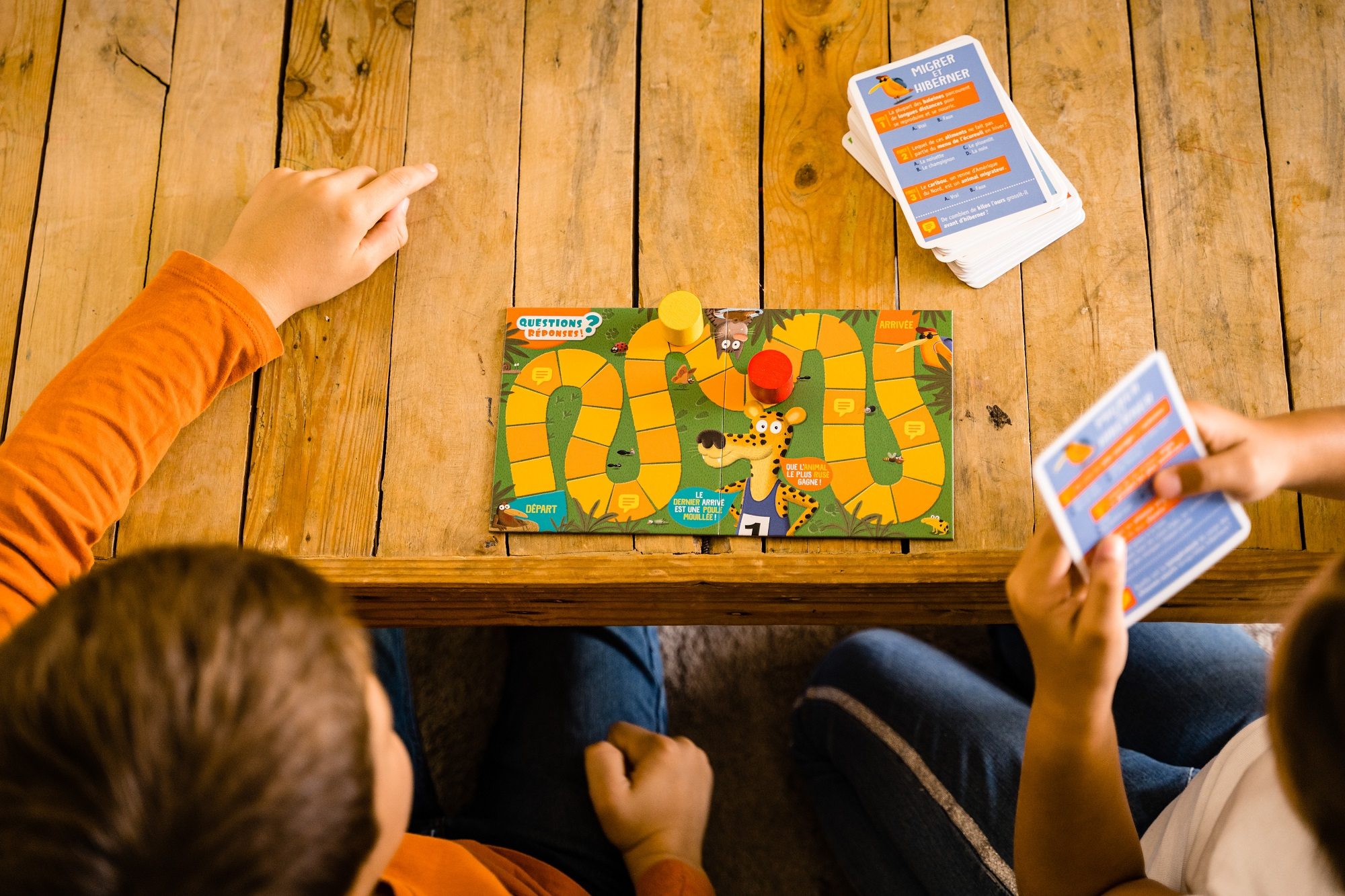 Dwoje dzieci grających w grę planszową z kartami na drewnianym stole.