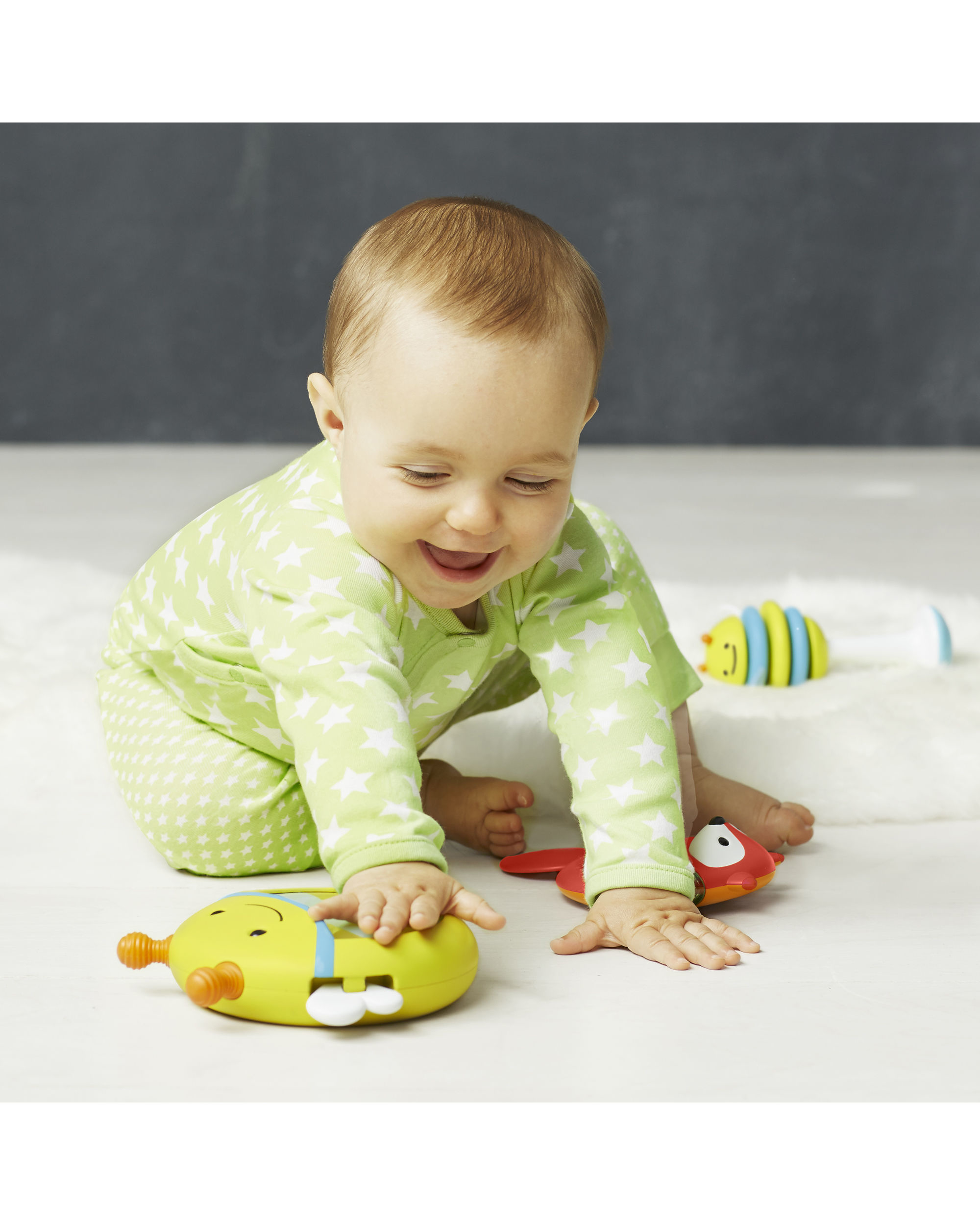 Baby greift nach Spielzeug. Spielzeug ist eine Biene, ein Fuchs und eine blau-gelbe Rassel.
