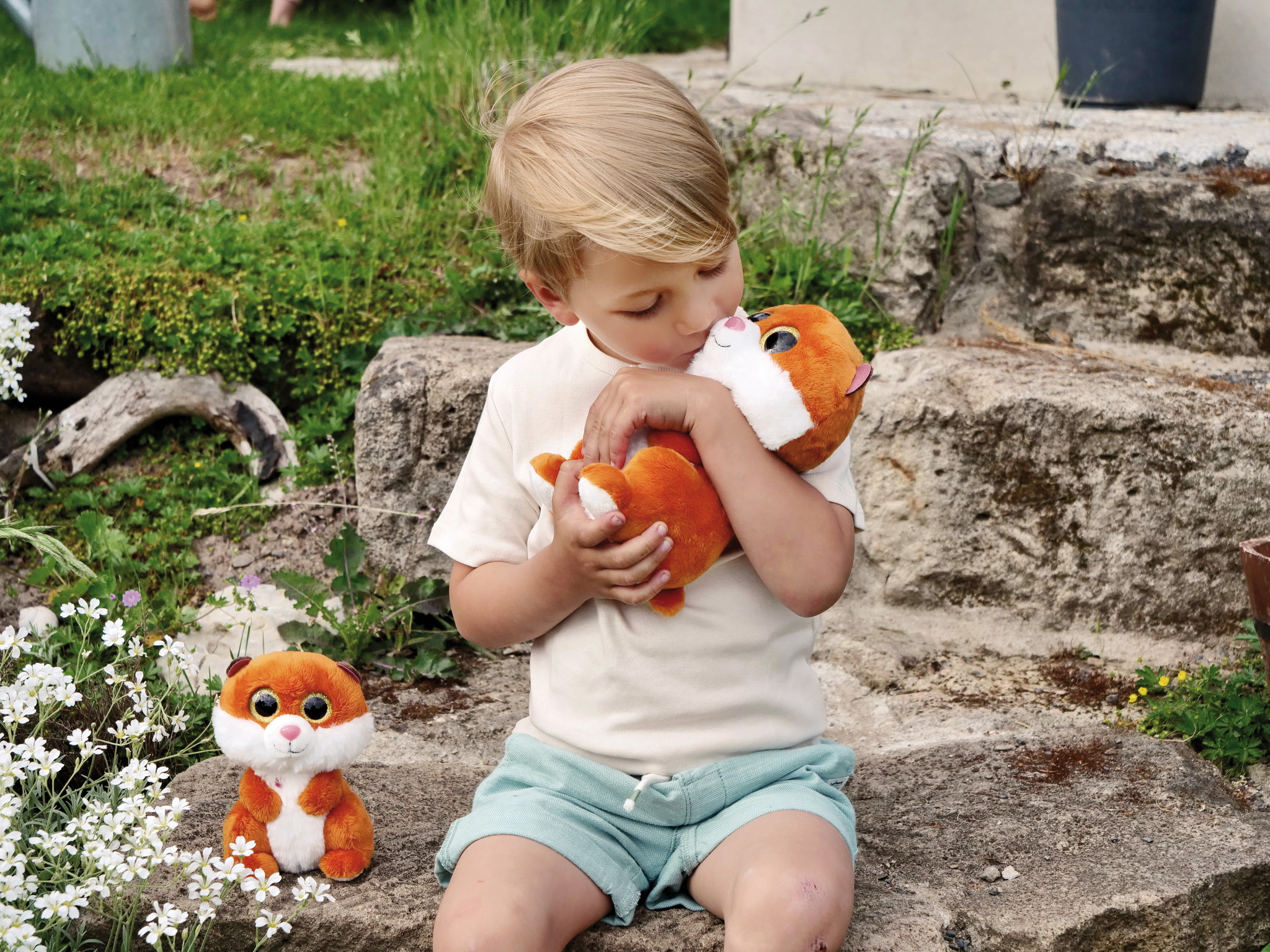 Mały chłopiec przytula pomarańczowego pluszowego lisa. Na ziemi kolejna zabawka z lisem.