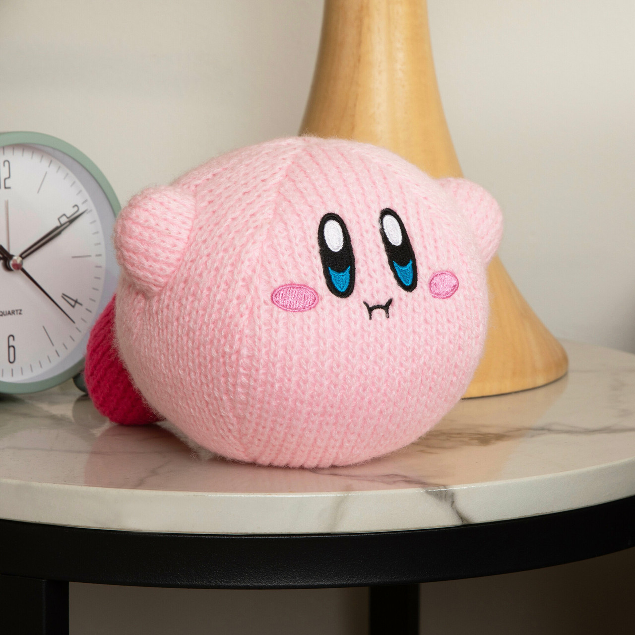 Un peluche di Kirby rosa lavorato a maglia con grandi occhi blu, seduto su un tavolo di marmo.