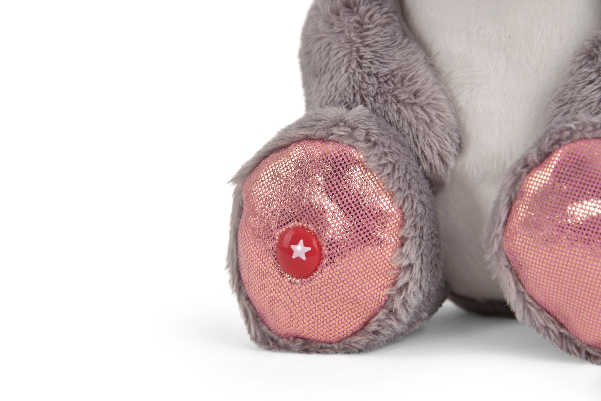 Zbliżenie na stopy pluszowej zabawki z różowymi, błyszczącymi podeszwami, czerwonym guzikiem w kształcie gwiazdy i szarym futrem.
