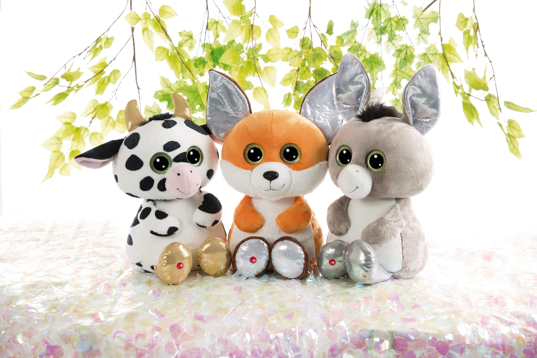 Drei Plüschtiere: eine Kuh mit schwarzen Flecken, ein orangefarbener Fuchs und ein grauer Esel, alle mit großen Augen und goldenen Akzenten.