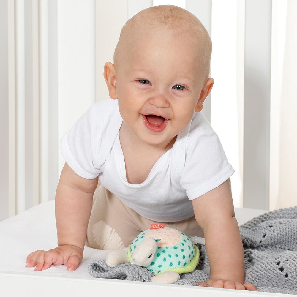 Dziecko uśmiecha się, pełzając w kierunku szarego koca i pluszowej żółwia.