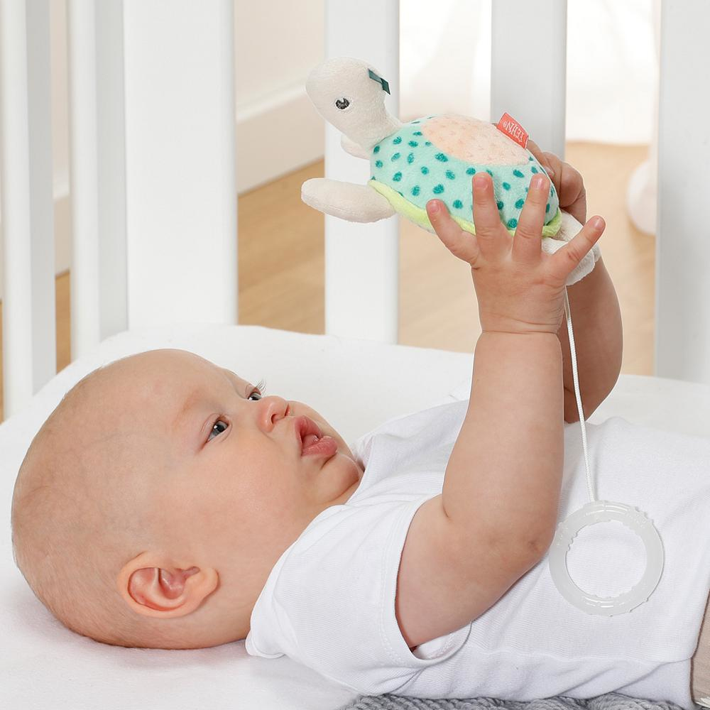 Dziecko trzymające pluszową żółwia leżąc na łóżku, białe tło.