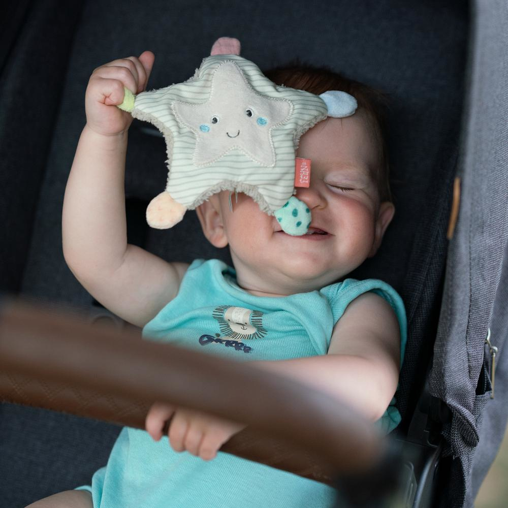 Dziecko uśmiecha się, trzymając zabawkę w kształcie gwiazdy w wózku.