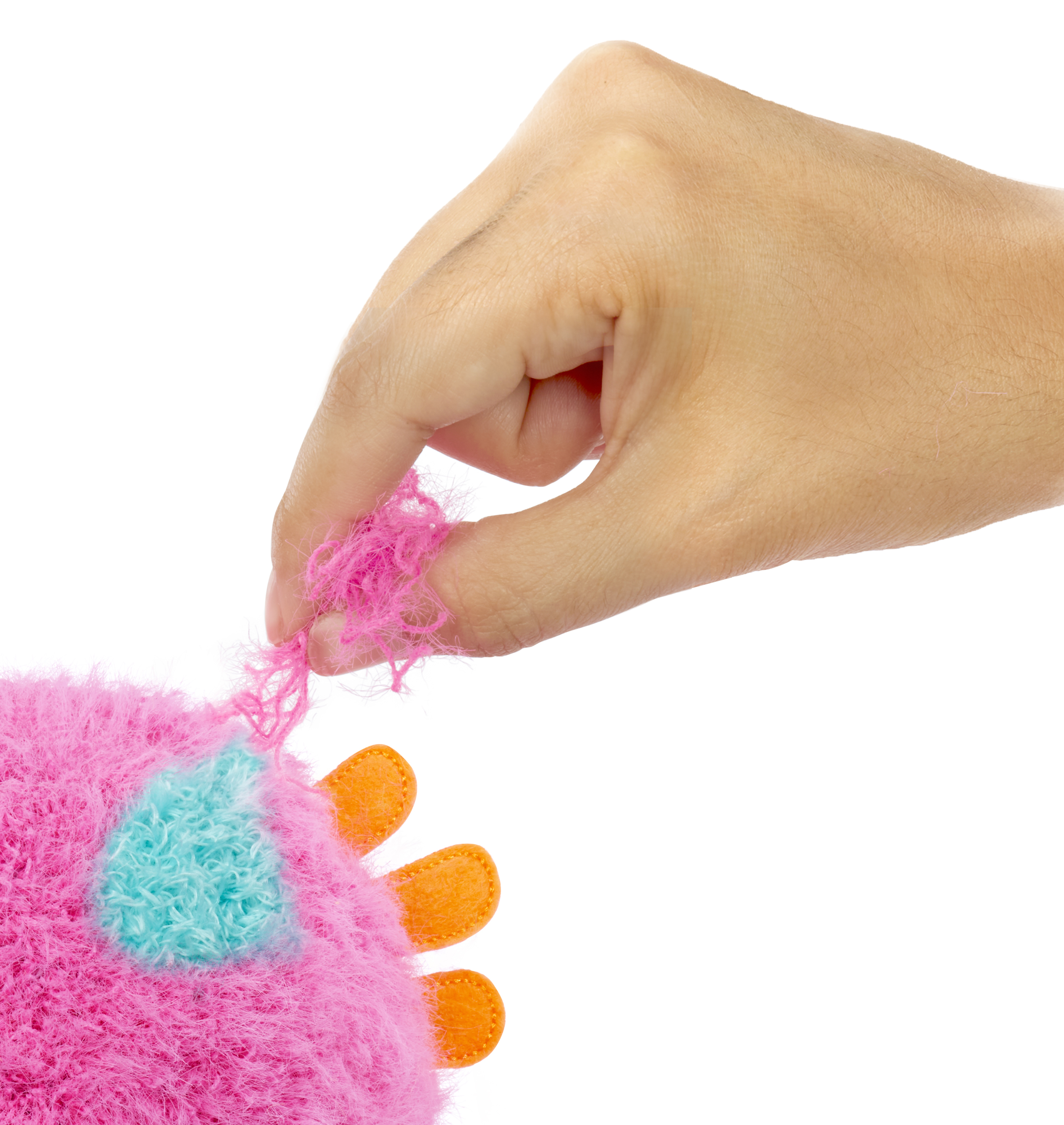 Dłoń wyciąga nitki z różowej, puszystej zabawki z niebieskimi i pomarańczowymi detalami na białym tle.