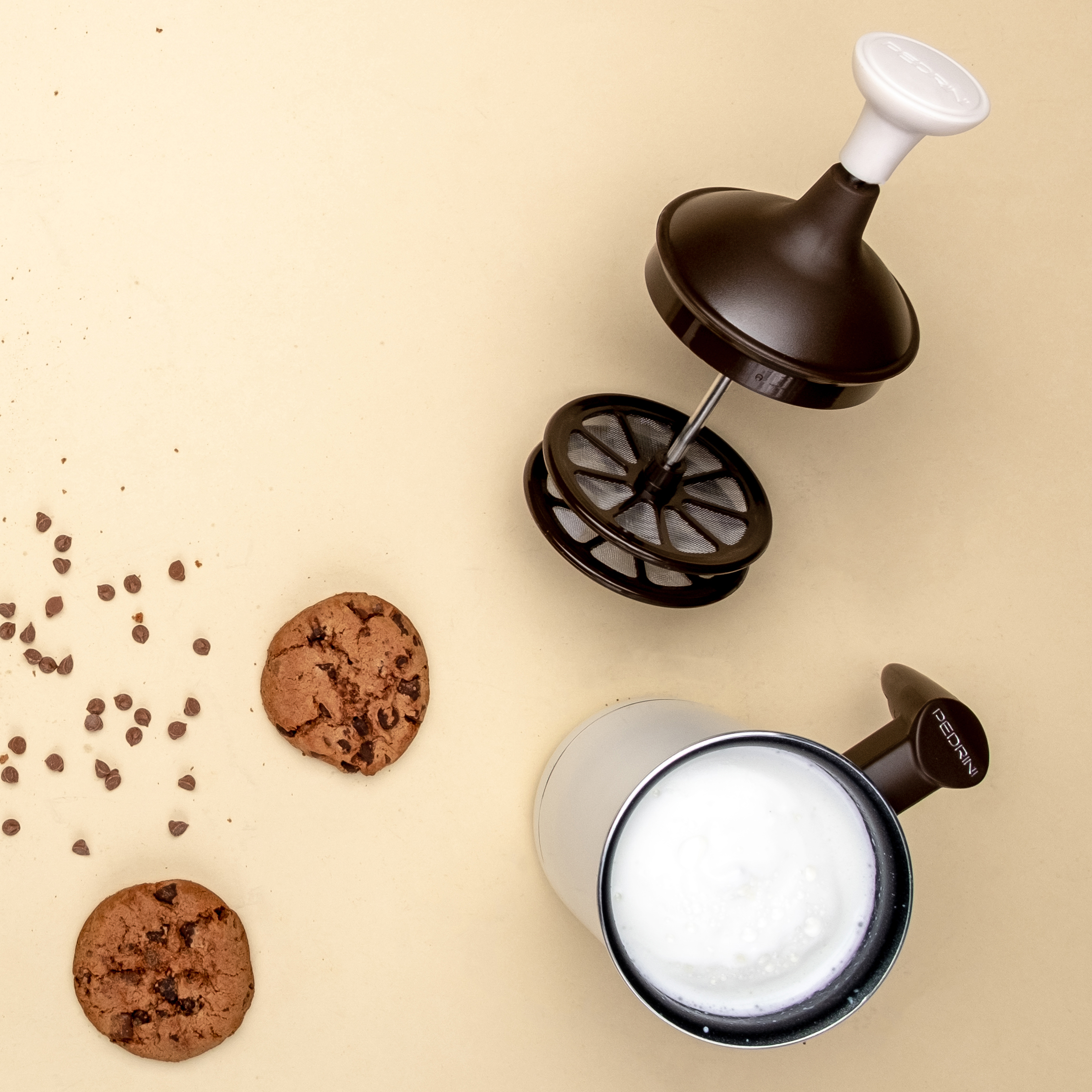 Due biscotti, una macchina per cappuccino e gocce di cioccolato su una superficie beige.