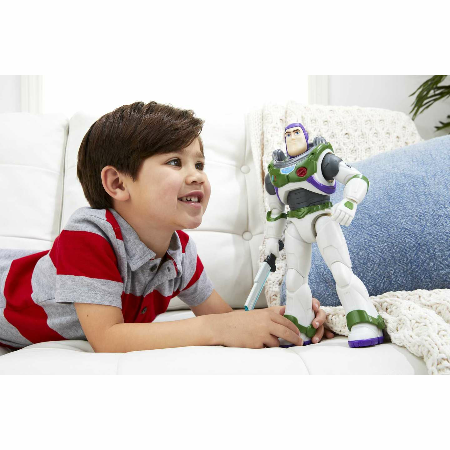 Ragazzo e giocattolo di Buzz Lightyear. Il ragazzo sorride mentre guarda Buzz. Cuscino blu, divano bianco sullo sfondo.