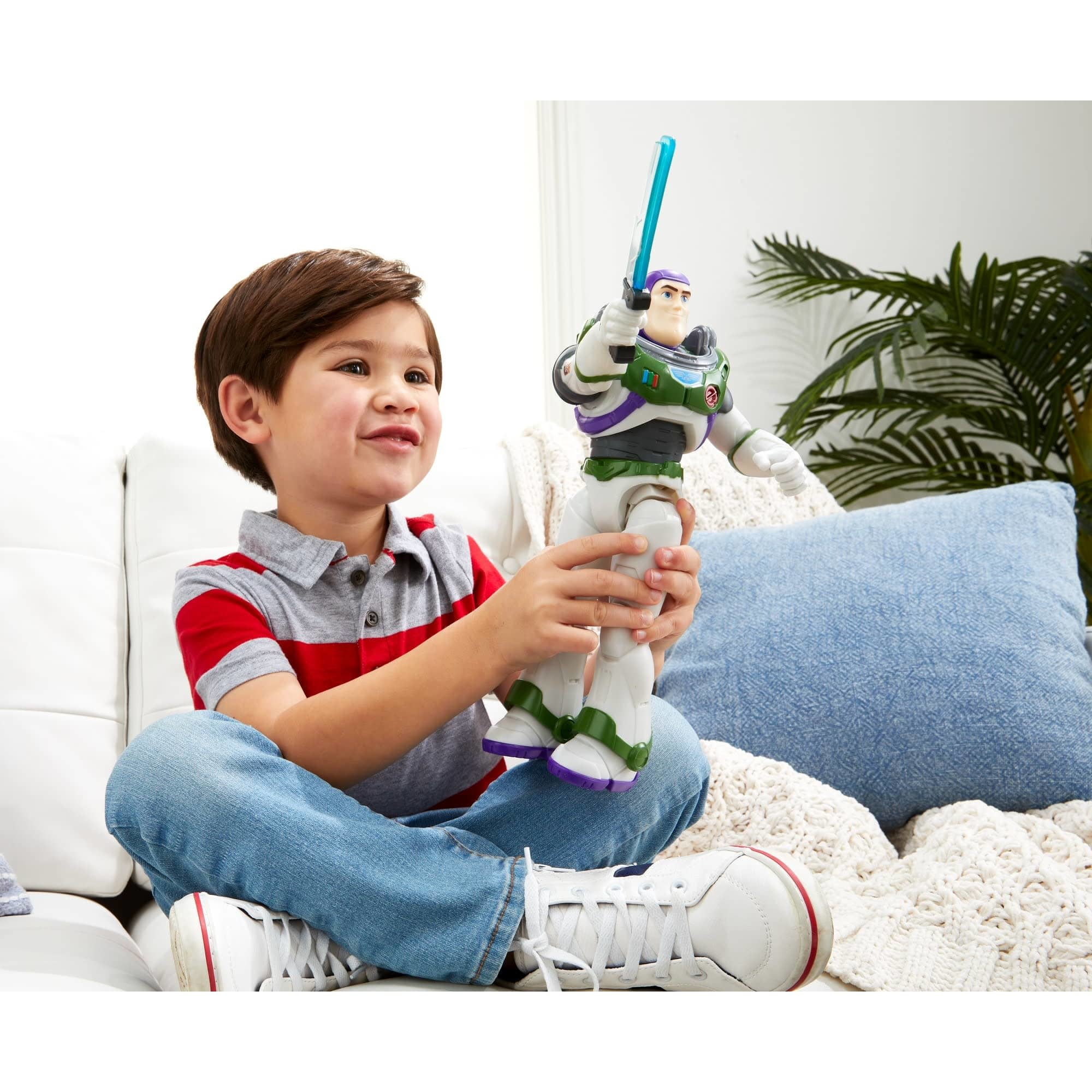 Ragazzo che gioca con un giocattolo di Buzz Lightyear. Il ragazzo sorride. Giocattolo che tiene una spada laser blu. Divano bianco sullo sfondo.