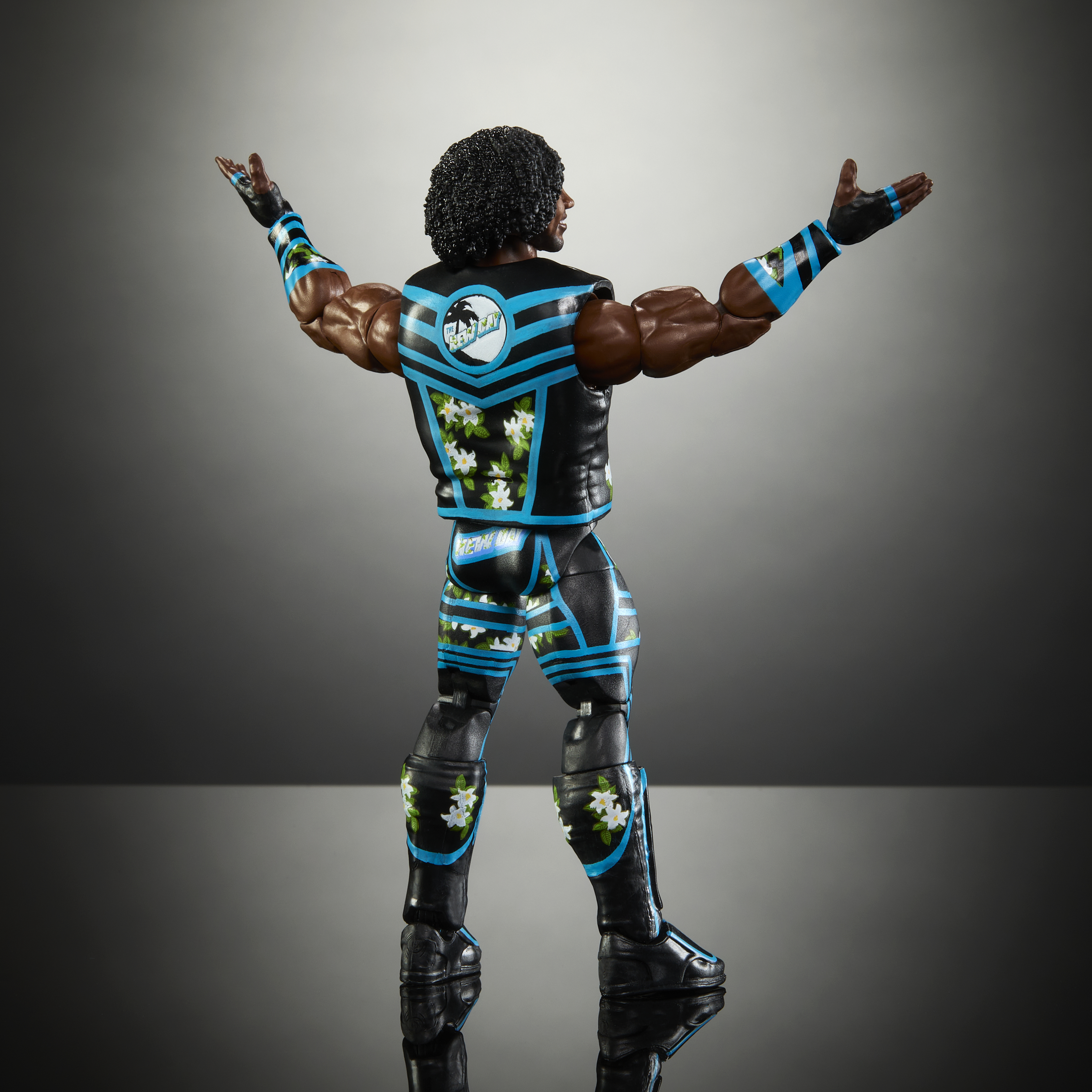 Wrestler-Figur in schwarz-blauer Ausrüstung, Arme ausgestreckt. Schwarze Haut, lockiges Haar, grauer Hintergrund.