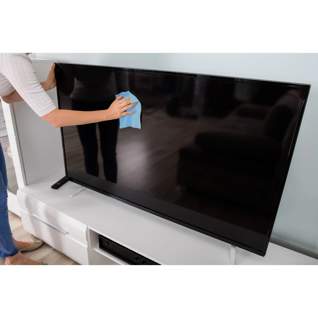 Una persona pulisce un grande schermo TV nero con un panno blu.