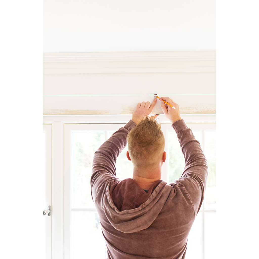 Eine Person verwendet einen Laserpegel, um eine Linie an der Wand zu markieren.