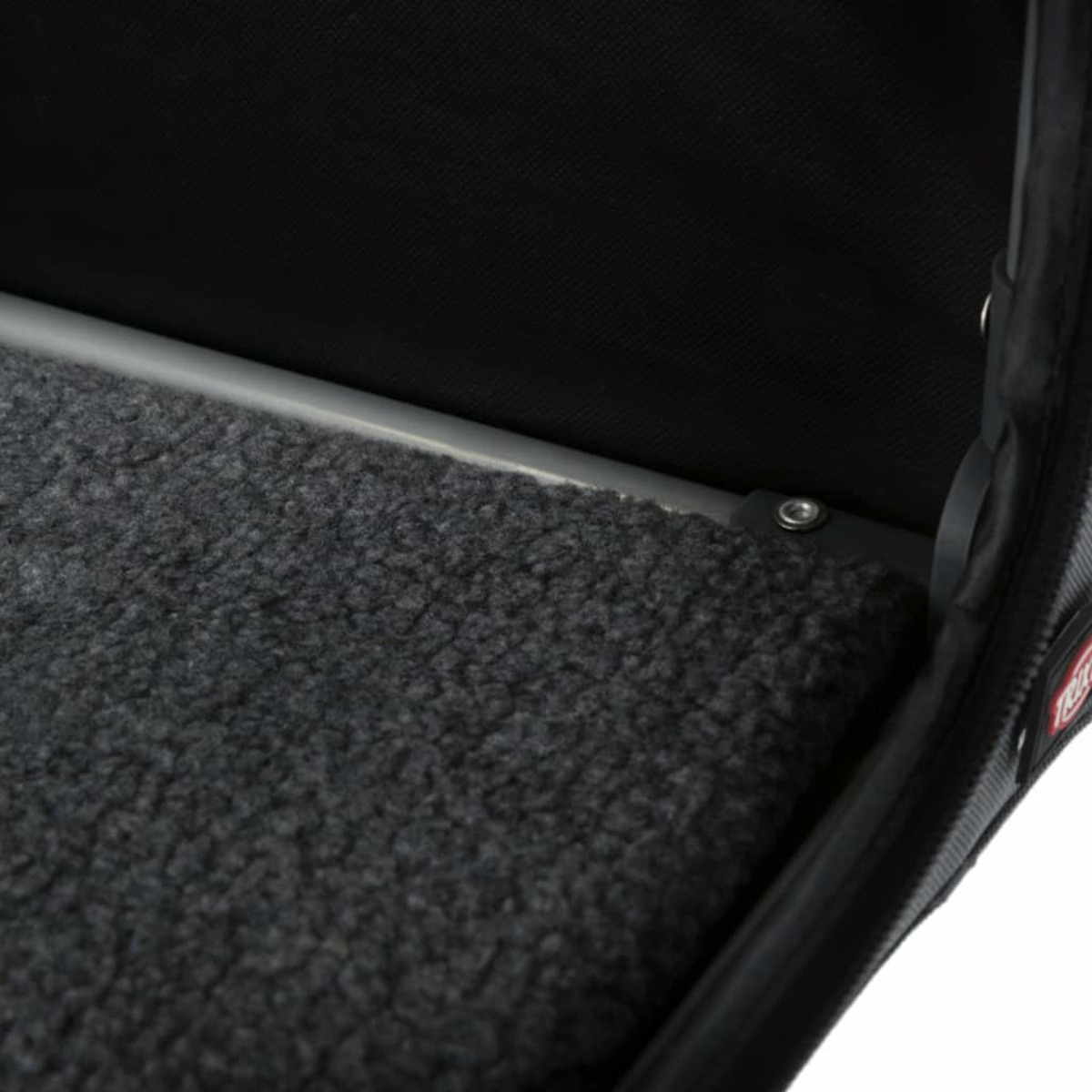 Zbliżenie wnętrza transportera dla zwierząt z szarą, puszystą matą, metalową ramą. Czarne wnętrze.