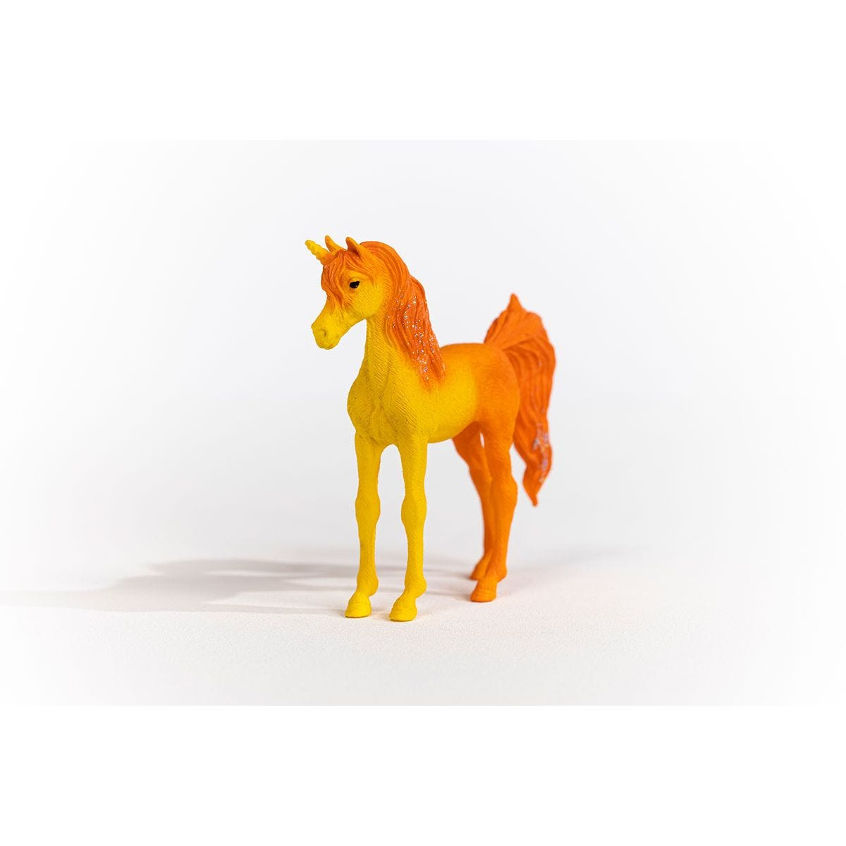 Ein gelbes und orangefarbenes Spielzeugpferd, das auf einer weißen Oberfläche steht.