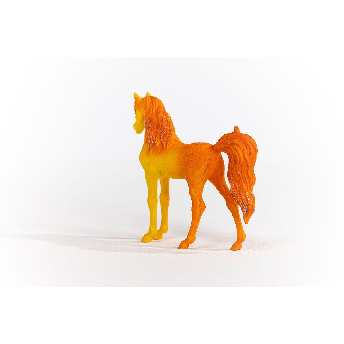 Ein Spielzeugpferd, orange und gelb, steht auf einer weißen Oberfläche. Es ist eine Rückansicht.