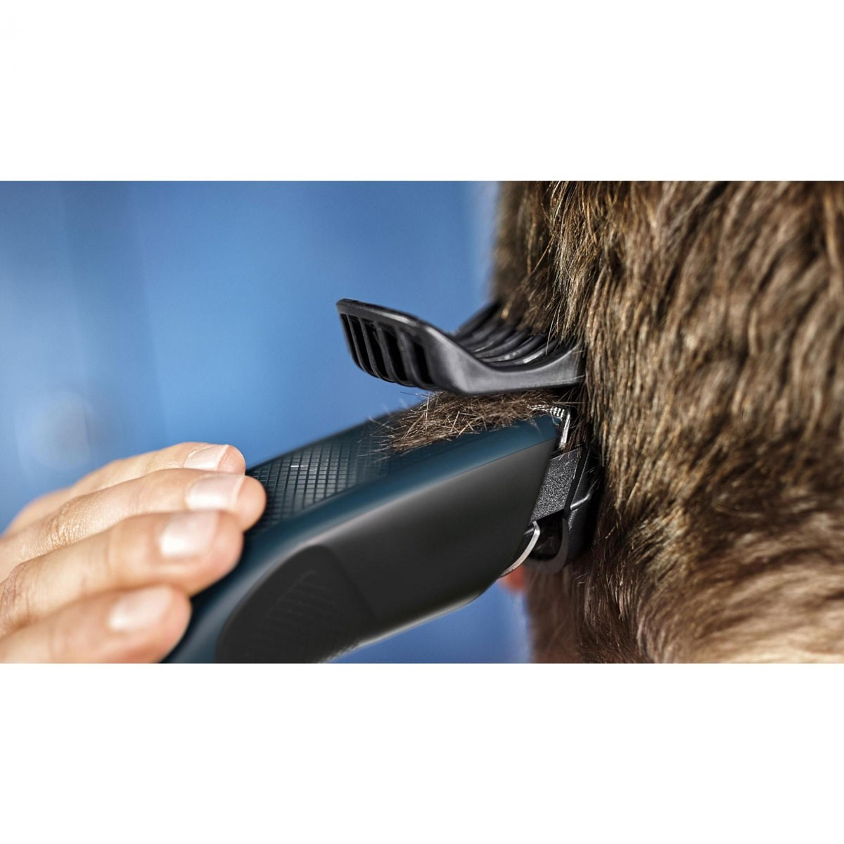 Eine Person schneidet Haare mit einem Haarschneider. Der Haarschneider ist schwarz und blau. Der Hintergrund ist blau.