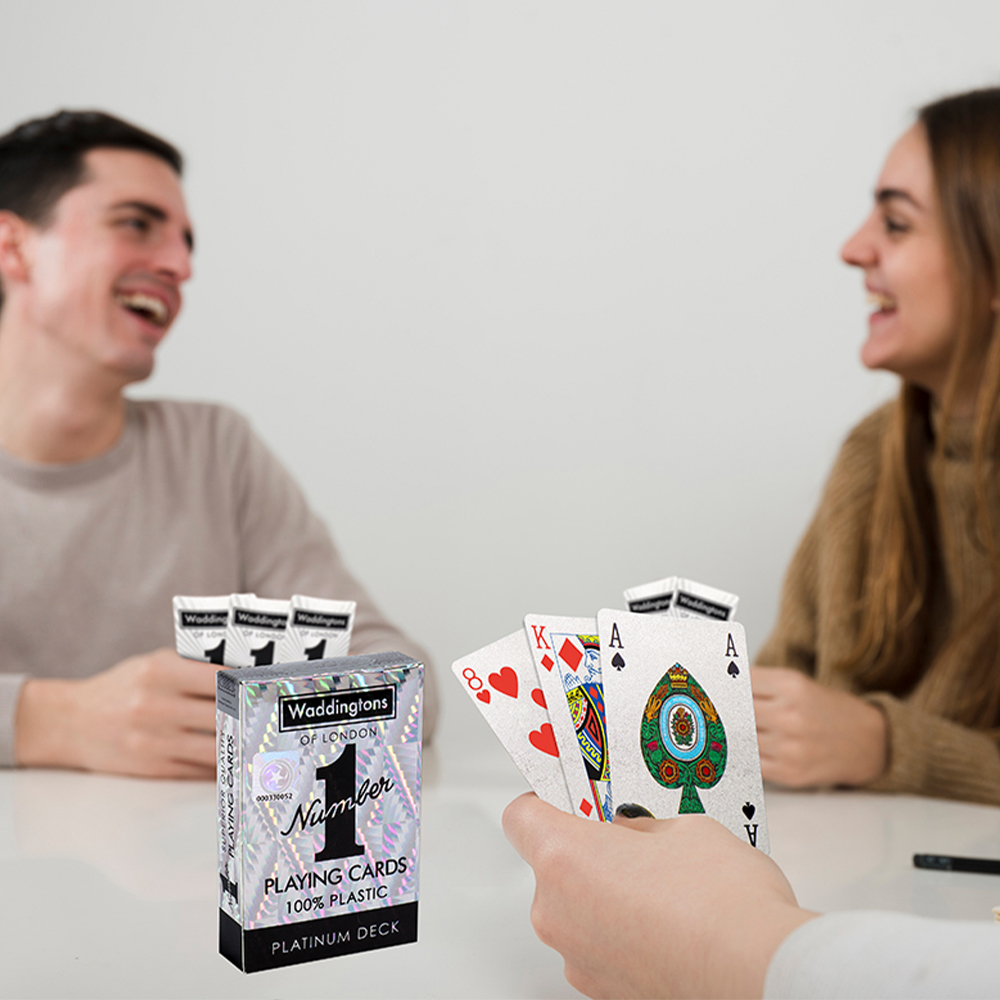 Des gens jouent aux cartes. Jeu de cartes sur la table. Cartes distribuées. Une boîte de cartes Waddington est visible.