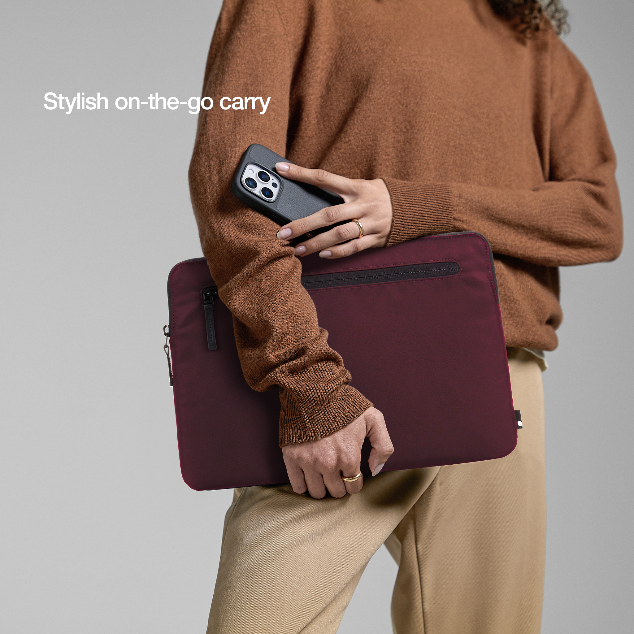 Una persona tiene in mano una custodia per laptop bordeaux con un telefono. Lo sfondo è semplice, con toni neutri.