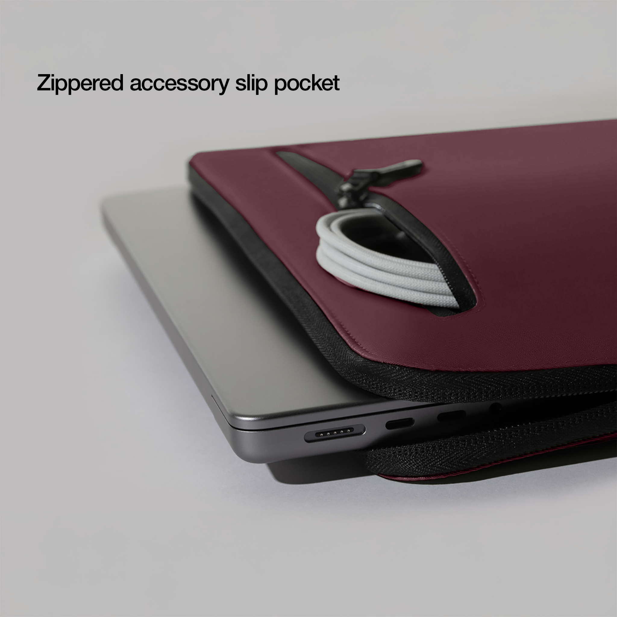 Un laptop e una custodia bordeaux, che mostra una tasca con cerniera, con un cavo di ricarica all'interno.