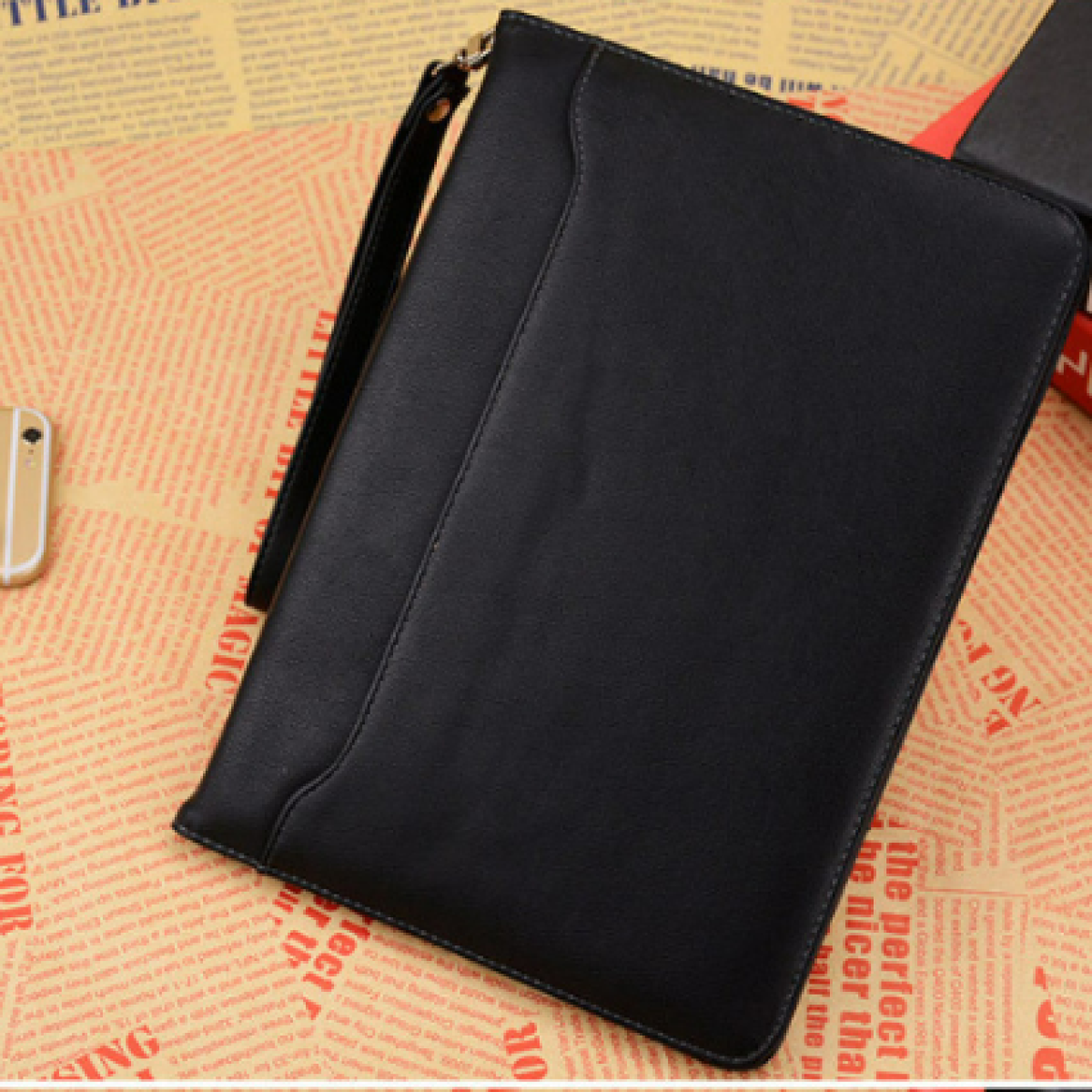 Custodia nera per tablet con cinturino da polso, su sfondo di giornale.