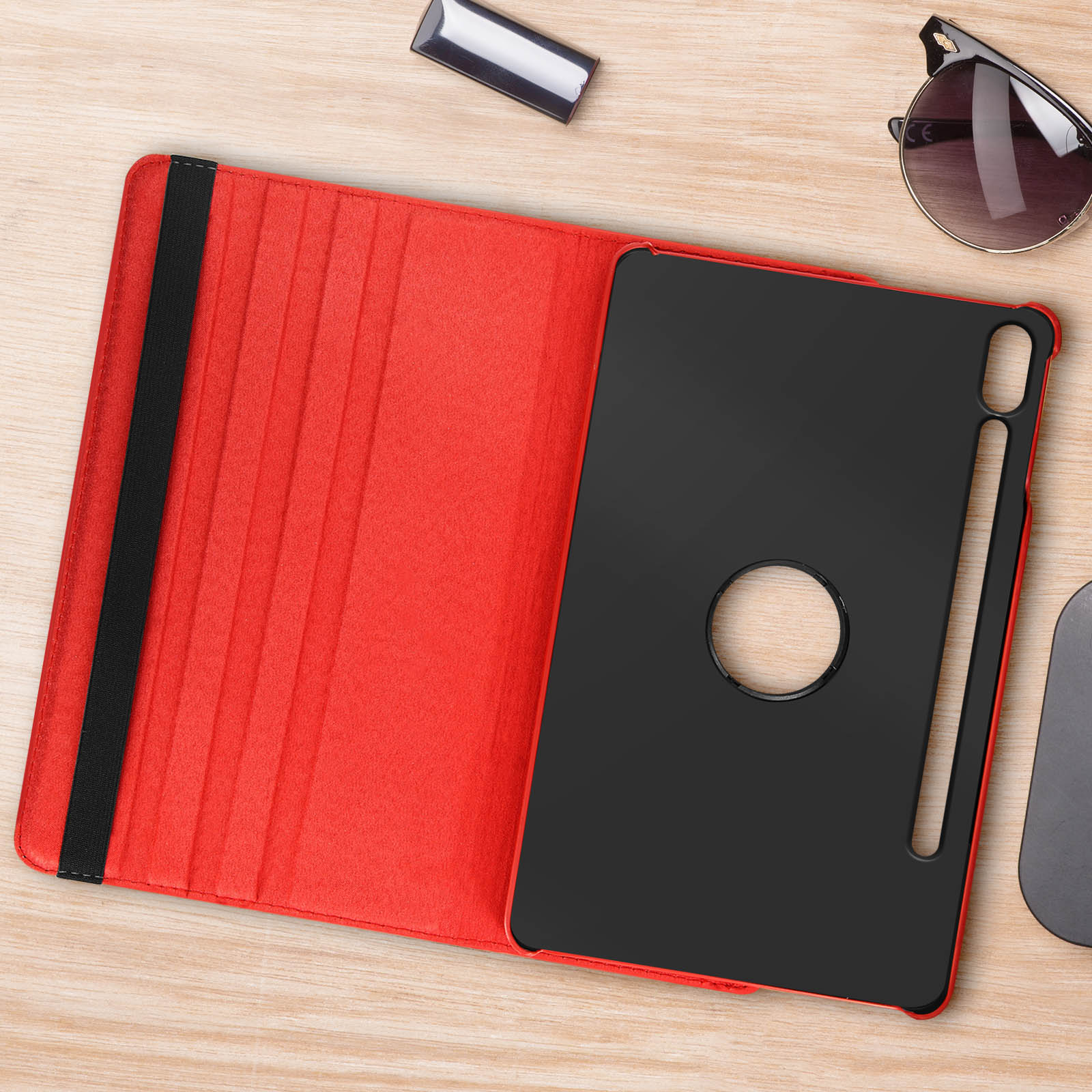 Custodia per tablet rossa aperta su una superficie in legno. Tablet nero all'interno. Occhiali da sole e penna nera sul lato.