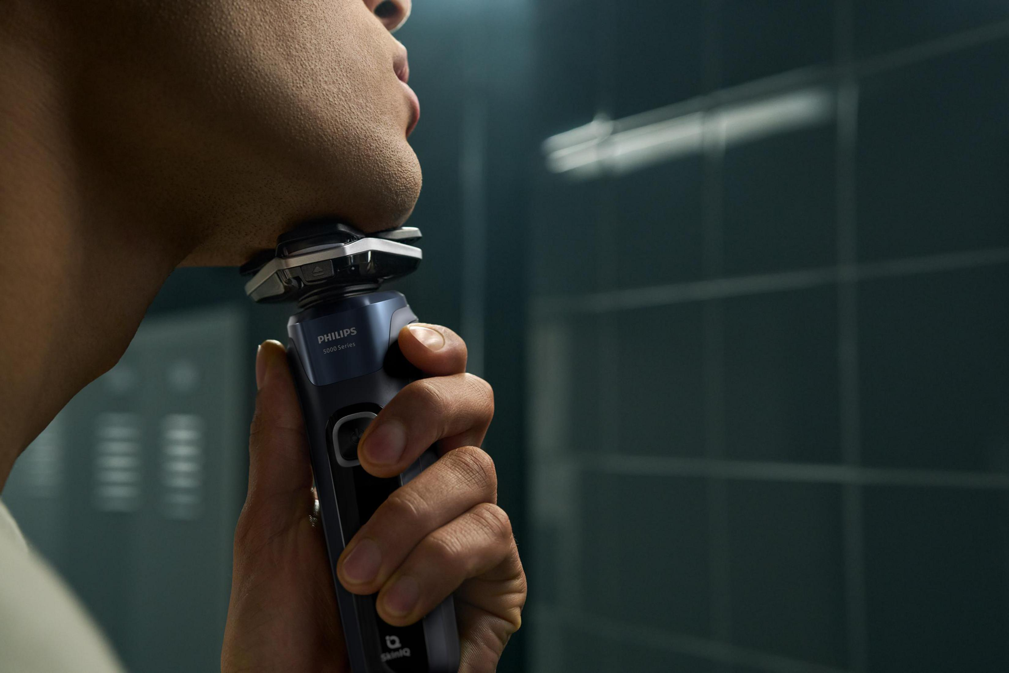 Primer plano de un hombre afeitándose con una afeitadora Philips. Espejo de baño detrás.