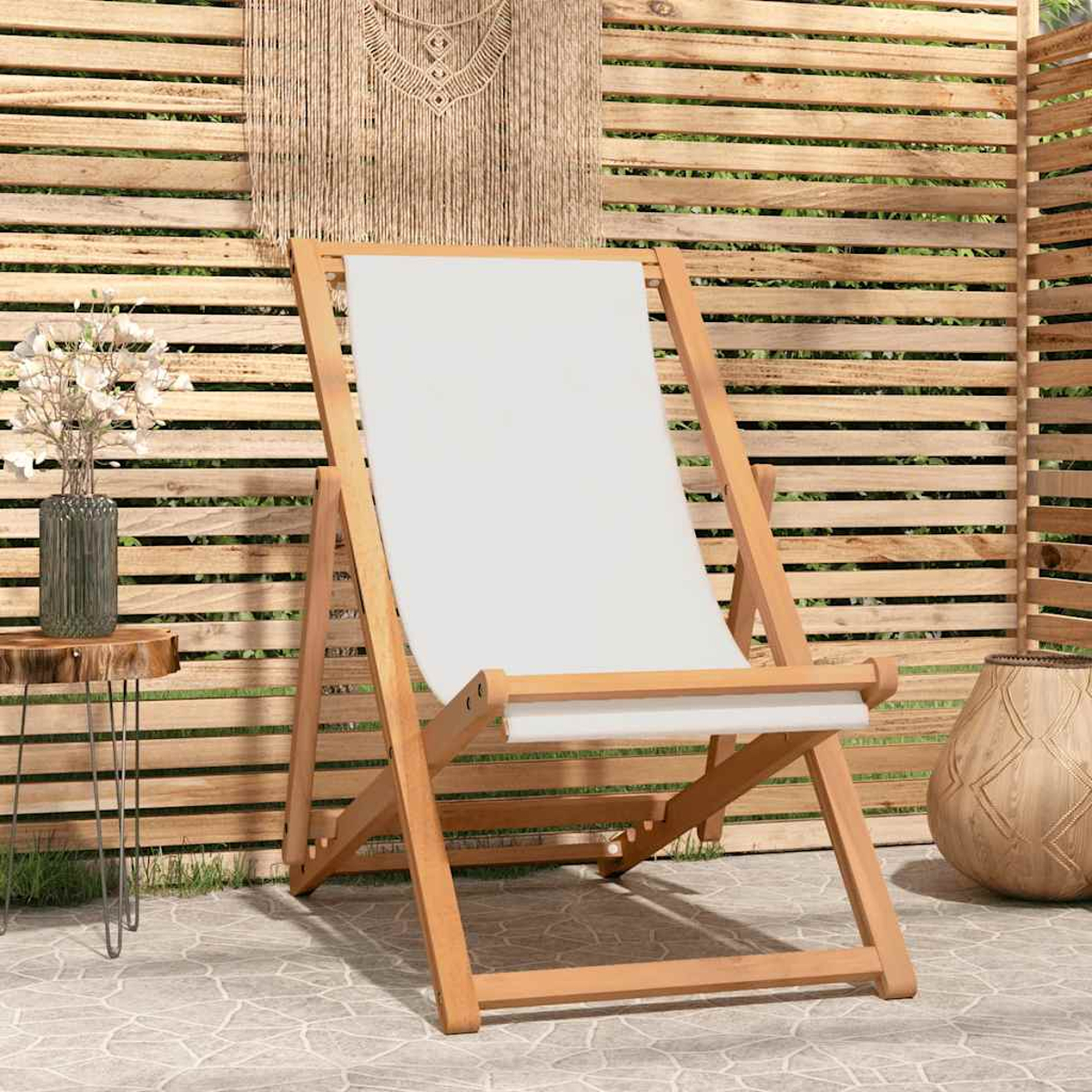 Klappbarer Holz-Deckchair mit weißem Stoffbezug steht auf einer Steinterrasse. Holzzaun im Hintergrund.