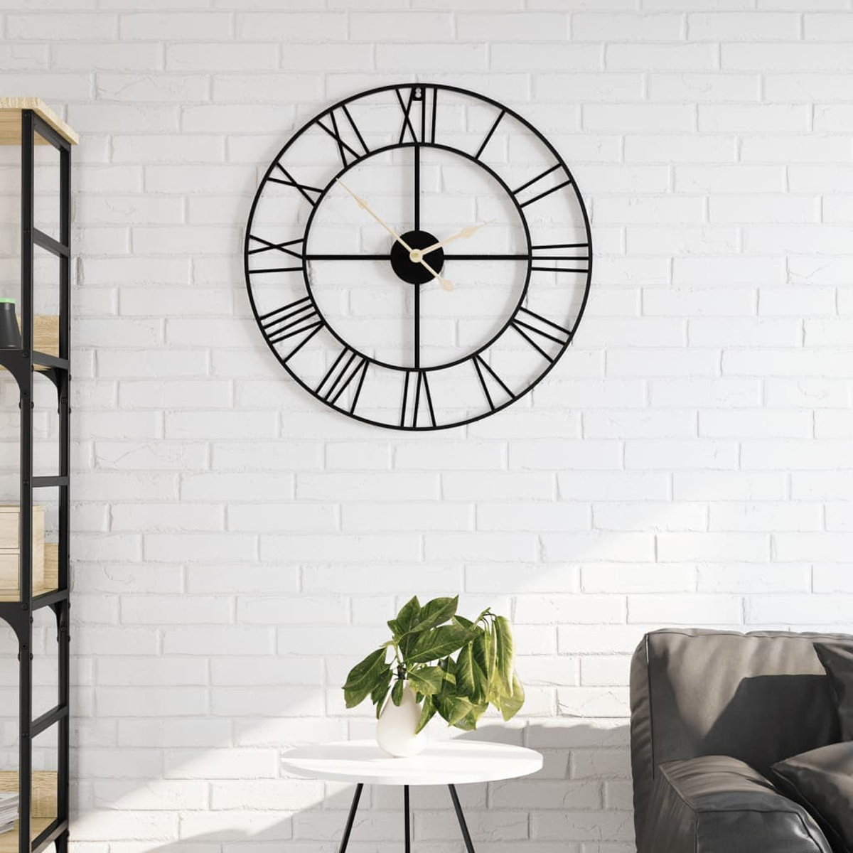 Schwarze Metall-Wanduhr mit römischen Ziffern an einer weißen Backsteinmauer. Auf einem Tisch steht eine Pflanze.