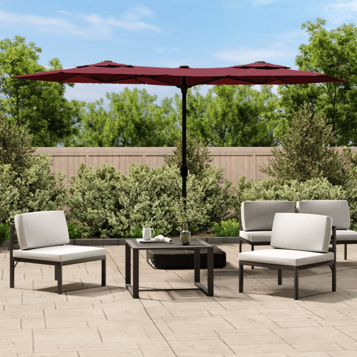 Eine Terrasse im Freien mit Möbeln und einem Doppel-Sonnenschirm. Grüne Büsche und blauer Himmel im Hintergrund.