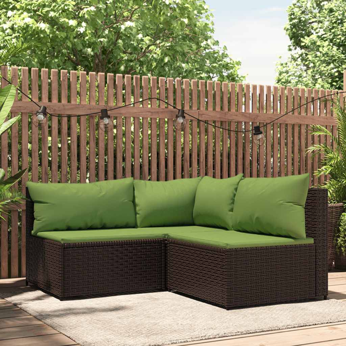 Ein braunes Ecksofa aus Korbgeflecht mit grünen Kissen auf einer Holzterrasse vor einem Holzzaun.