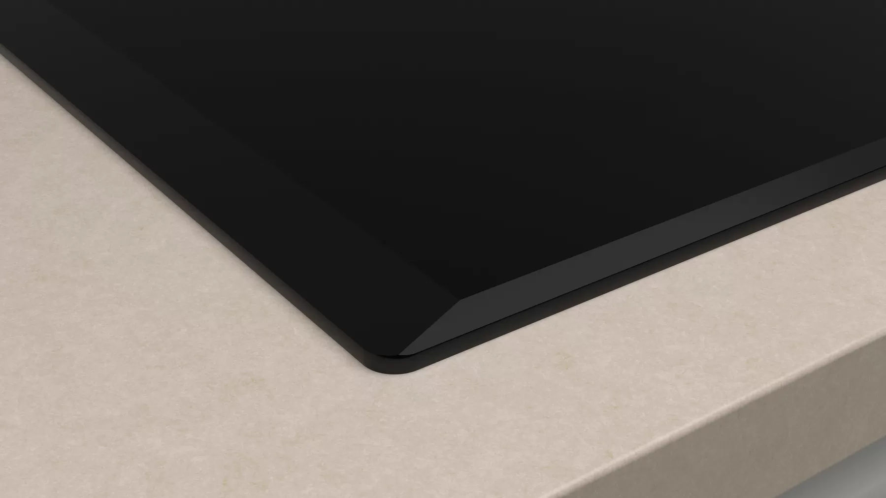 Zbliżenie krawędzi czarnej płyty grzewczej na jasnym blacie.