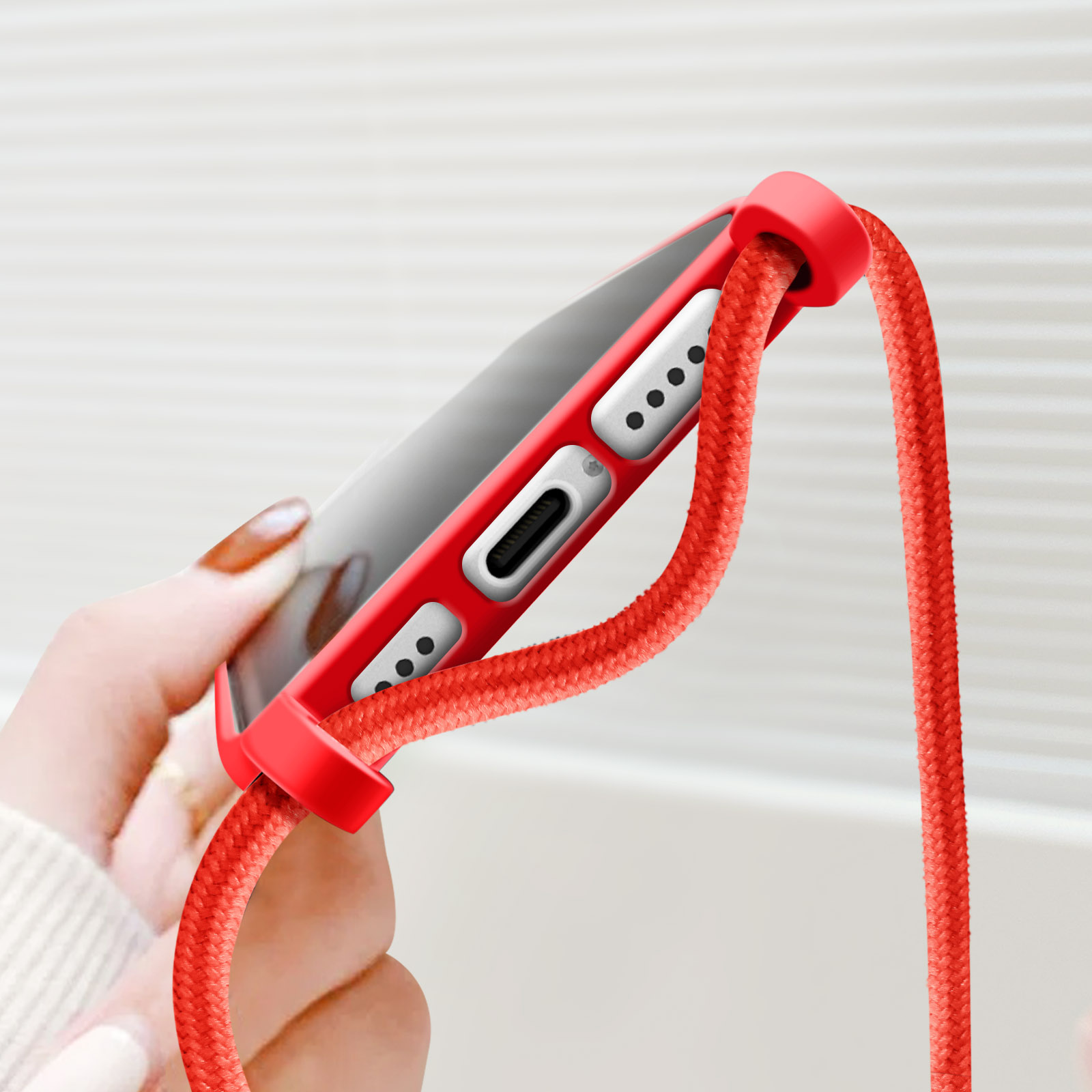 Persona che tiene una custodia per telefono rossa con un cordino rosso. Il telefono ha una porta di ricarica.