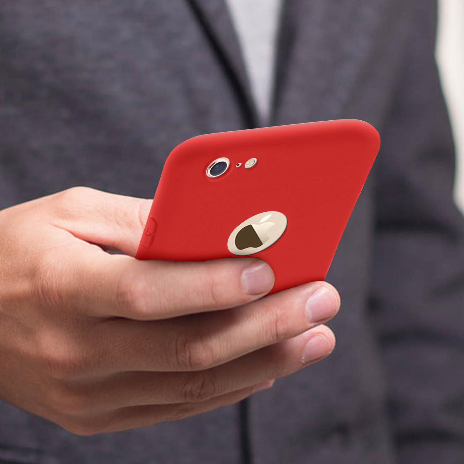 Mano sosteniendo un teléfono rojo con el logo plateado de Apple. Fondo de traje gris.