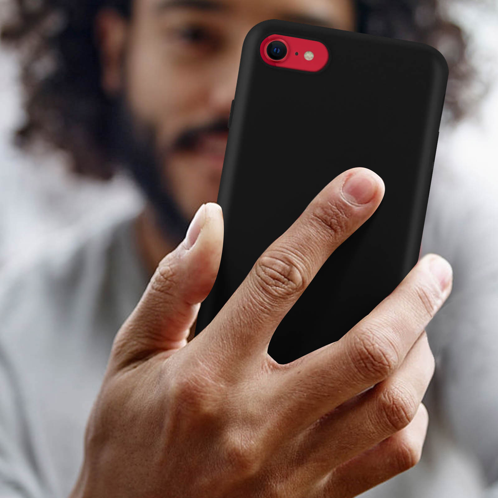 Uomo che tiene un telefono con custodia nera. Anello fotocamera rosso visibile.