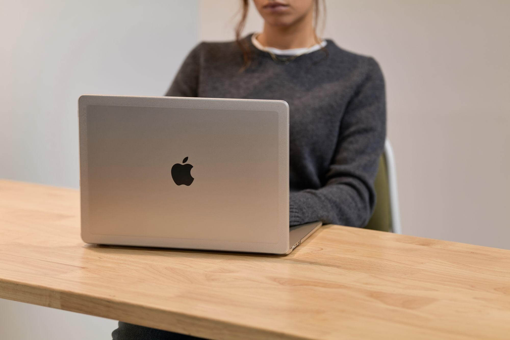 Persona che lavora su un laptop argentato a una scrivania di legno.
