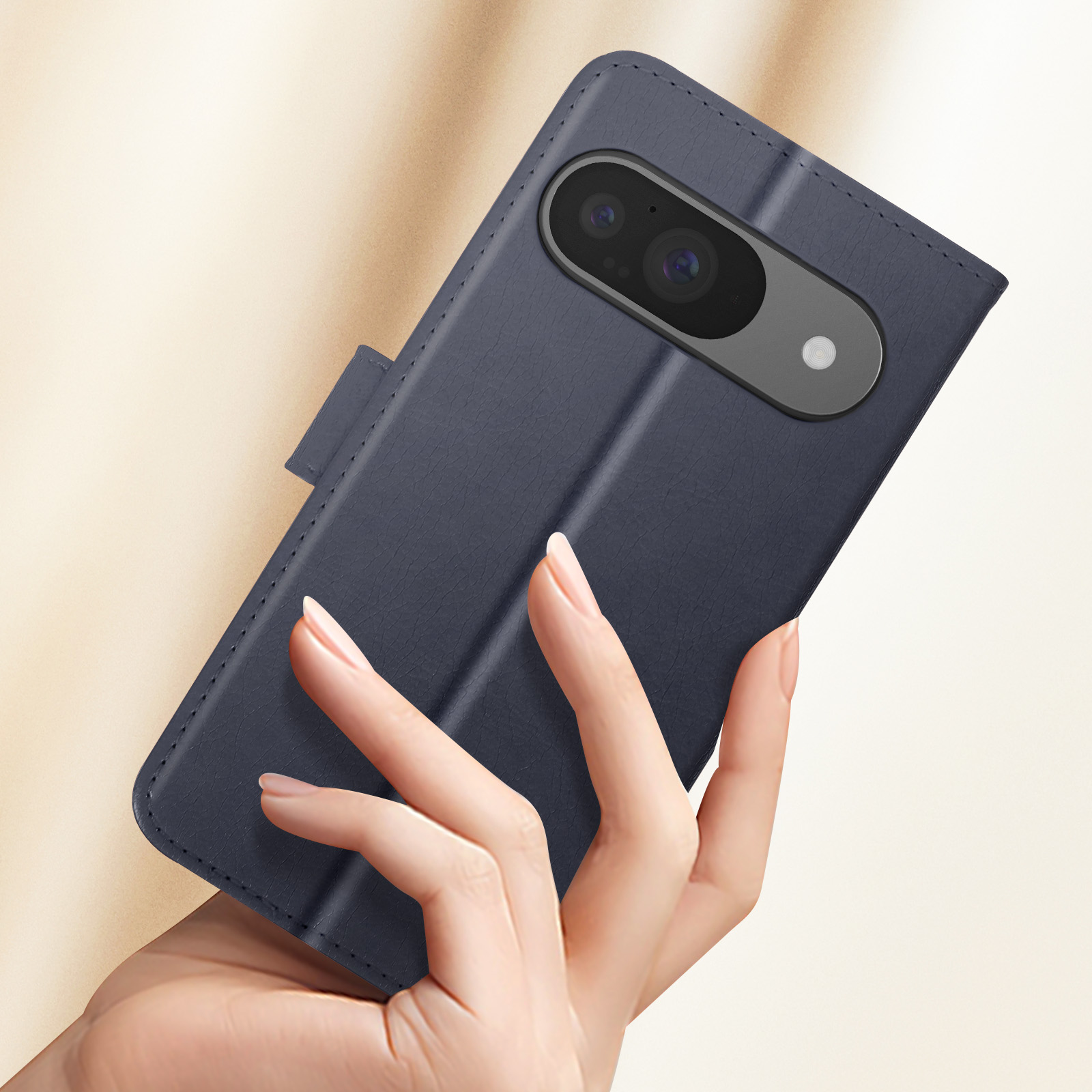 Mano che tiene una custodia blu navy con telefono e fotocamera. Lo sfondo è beige sfocato.