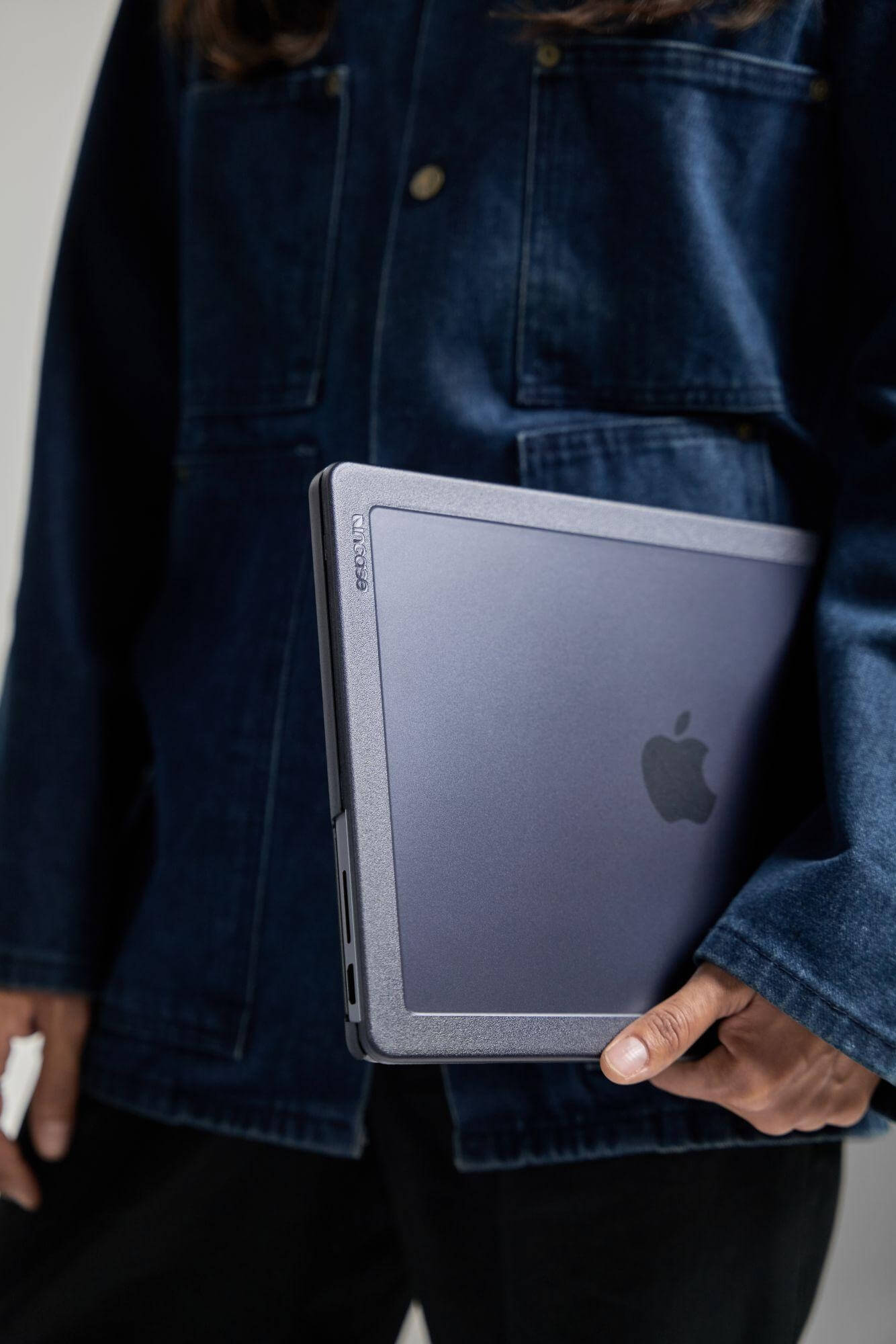 Person in Jeansjacke hält ein dunkelgraues Tablet mit Apple-Logo, vor weißem Hintergrund.