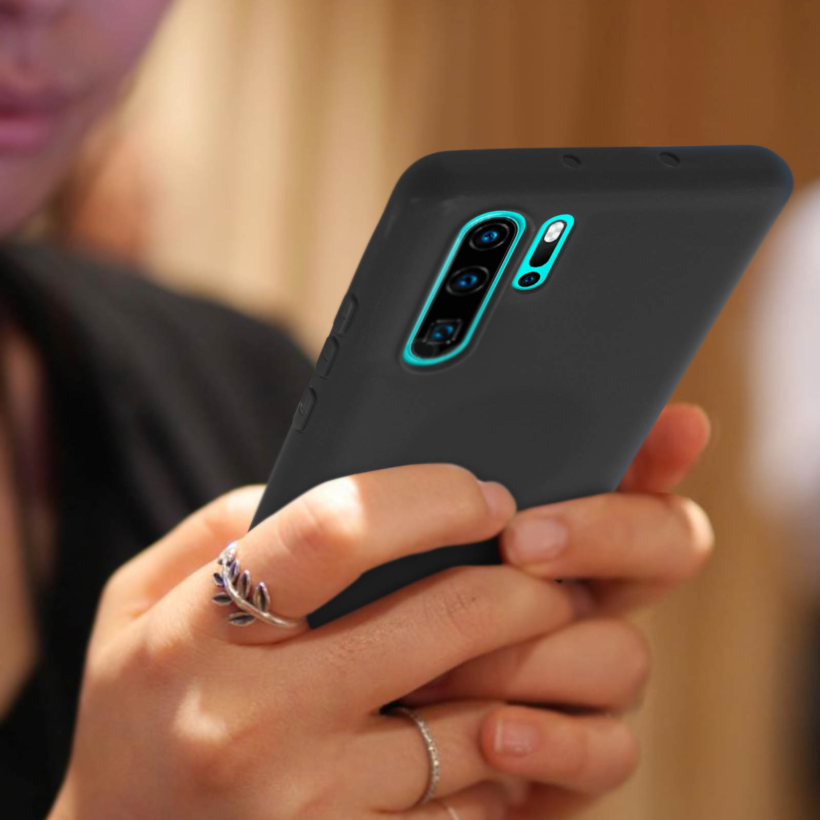 Telefono nero in custodia nera, tenuto da una persona con un anello. Fotocamera visibile.