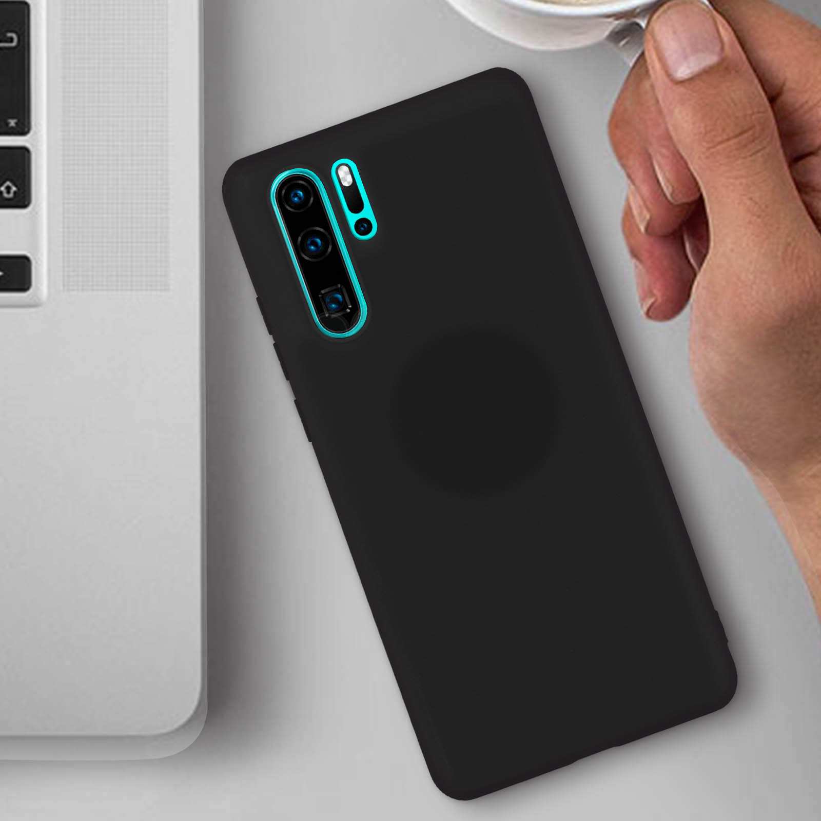 Custodia nera per telefono su tavolo bianco accanto a un laptop e una mano con una tazza.