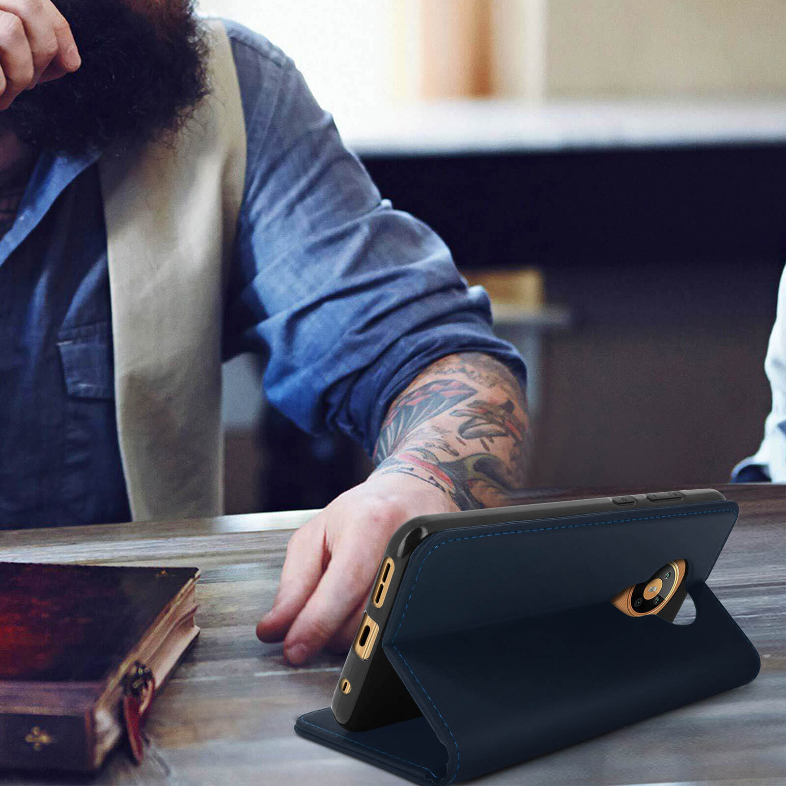 Un uomo è al telefono con una custodia blu scuro. C'è anche un libro sul tavolo.