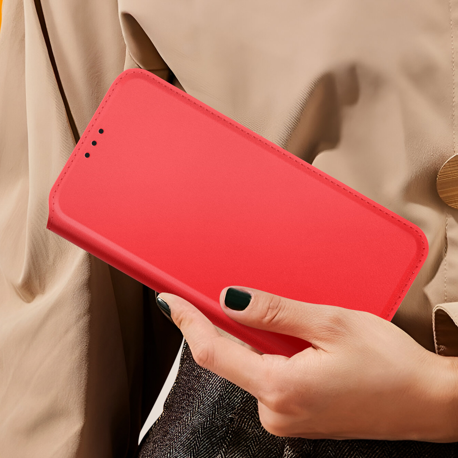Mano di una persona che tiene una custodia rossa per telefono. Abiti beige sullo sfondo. Unghie verde scuro.