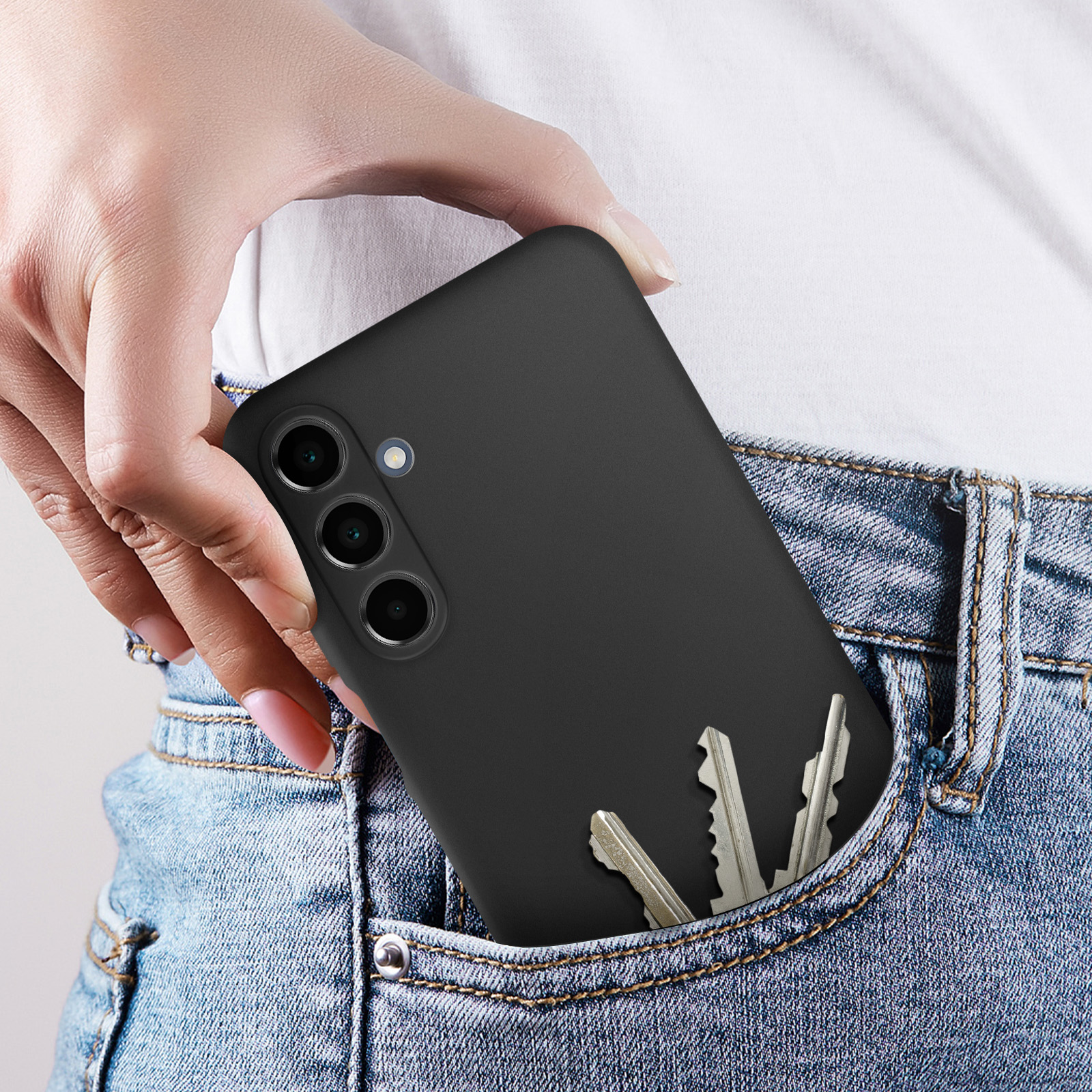 Un telefono nero con custodia in una tasca dei jeans. Le chiavi sono visibili. Camicia bianca e jeans blu.